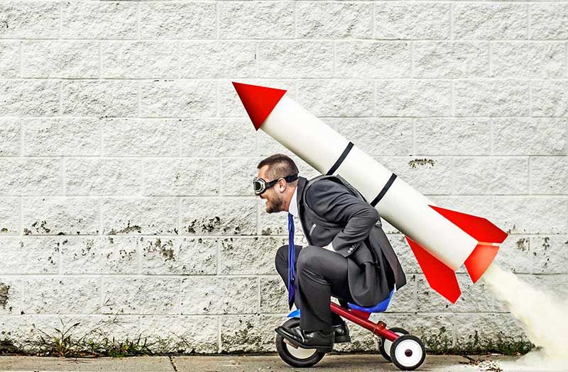 Business man sitting on bike with rocket strapped to his back